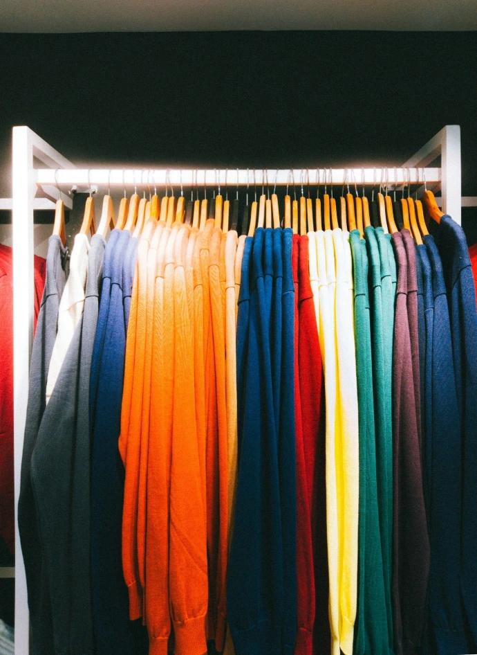a rack of colorful shirts hanging in a closet